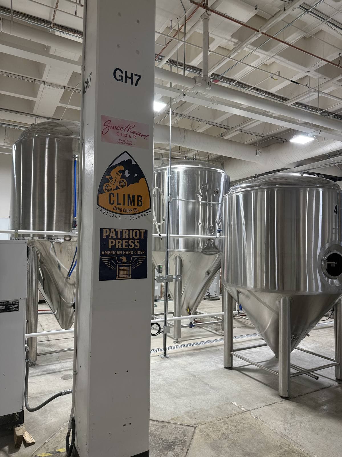 Stainless fermentation tanks beside a labeled cellar column on the Sweet Heart production floor